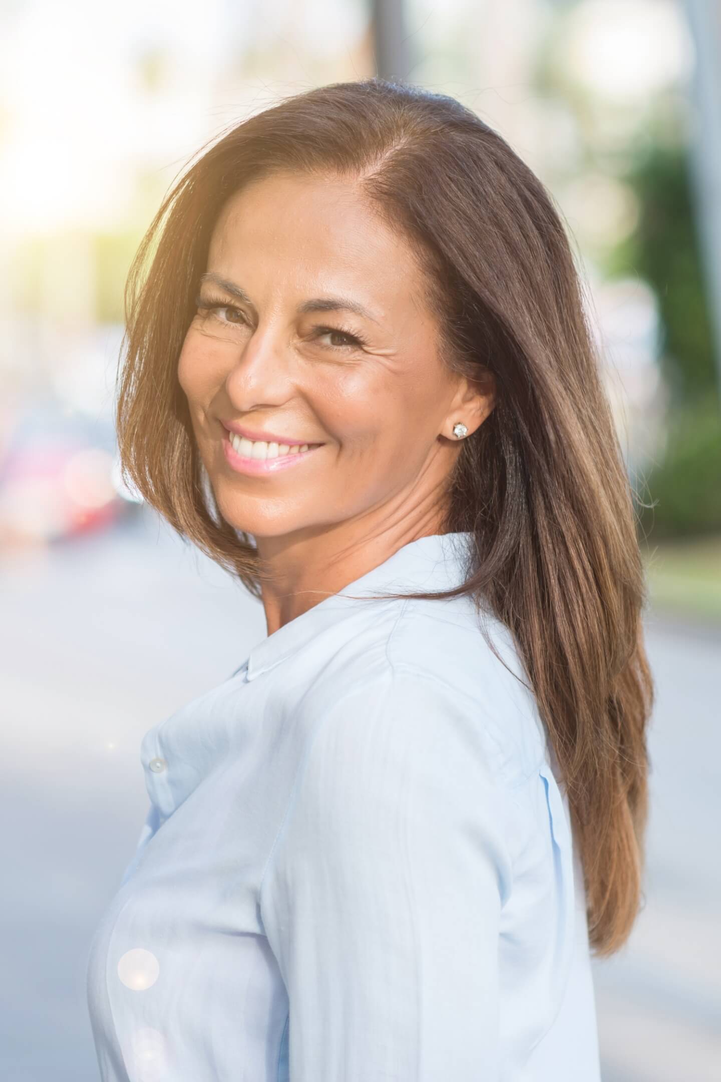 Mature woman wearing a light blue collared shirt looking over her shoulder